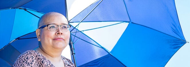 A woman undergoing chemotherapy holds a blue umbrella