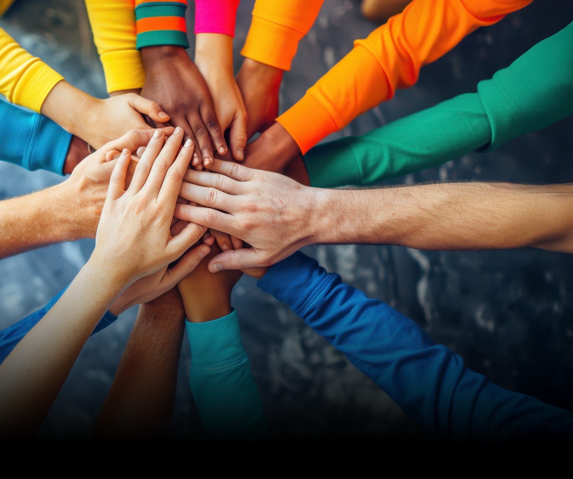 Hands stacked in a circle by people wearing colorful shirts, symbolizing teamwork.