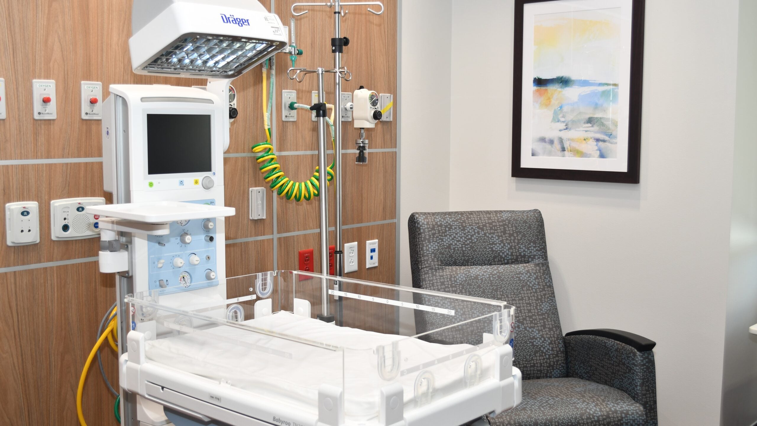 Hospital neonatal room with infant bassinet, monitor, and medical equipment.