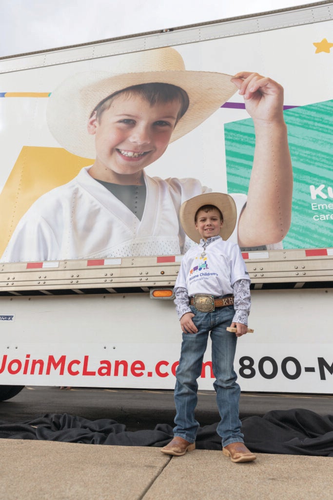 Wearing his signature cowboy hat, Kutter poses proudly in front of his larger‑than‑life photo.