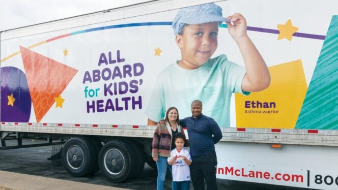 Colorful semi‑truck promoting kids’ health with the message ‘All aboard for kids’ health,’ as a family stands in front of the trailer.