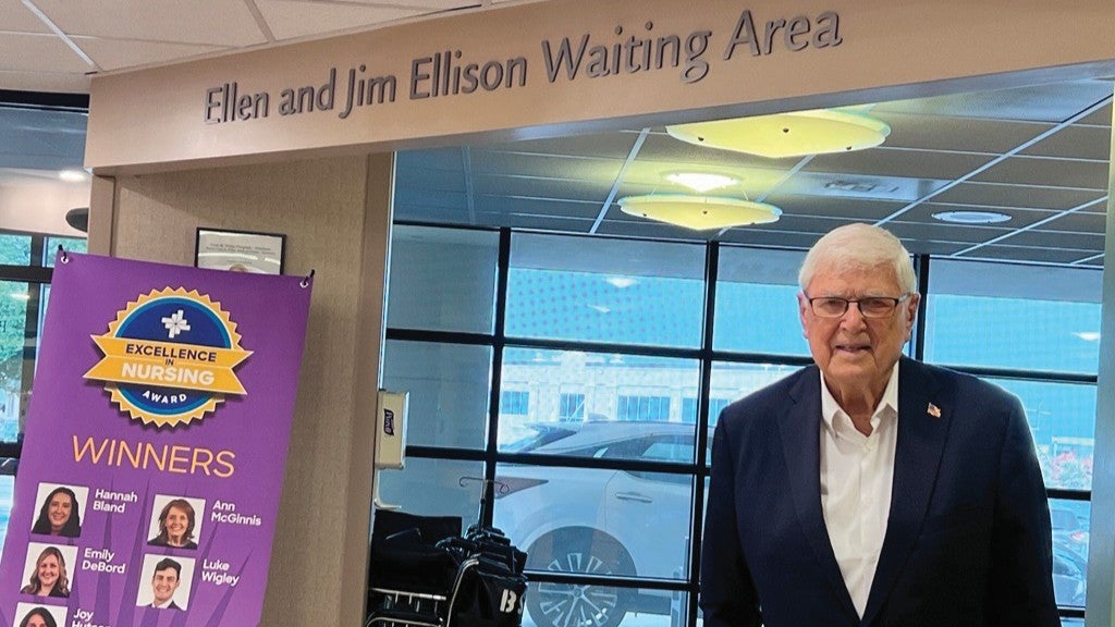 Sign reading “Ellen and Jim Ellison Waiting Area” inside a Baylor Scott & White facility, with a donor standing nearby and a nursing excellence award display in the background.