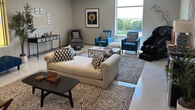 A bright, modern lounge with sofas, armchairs, a massage chair, patterned rugs and soft lighting, designed as a calm, welcoming space.
